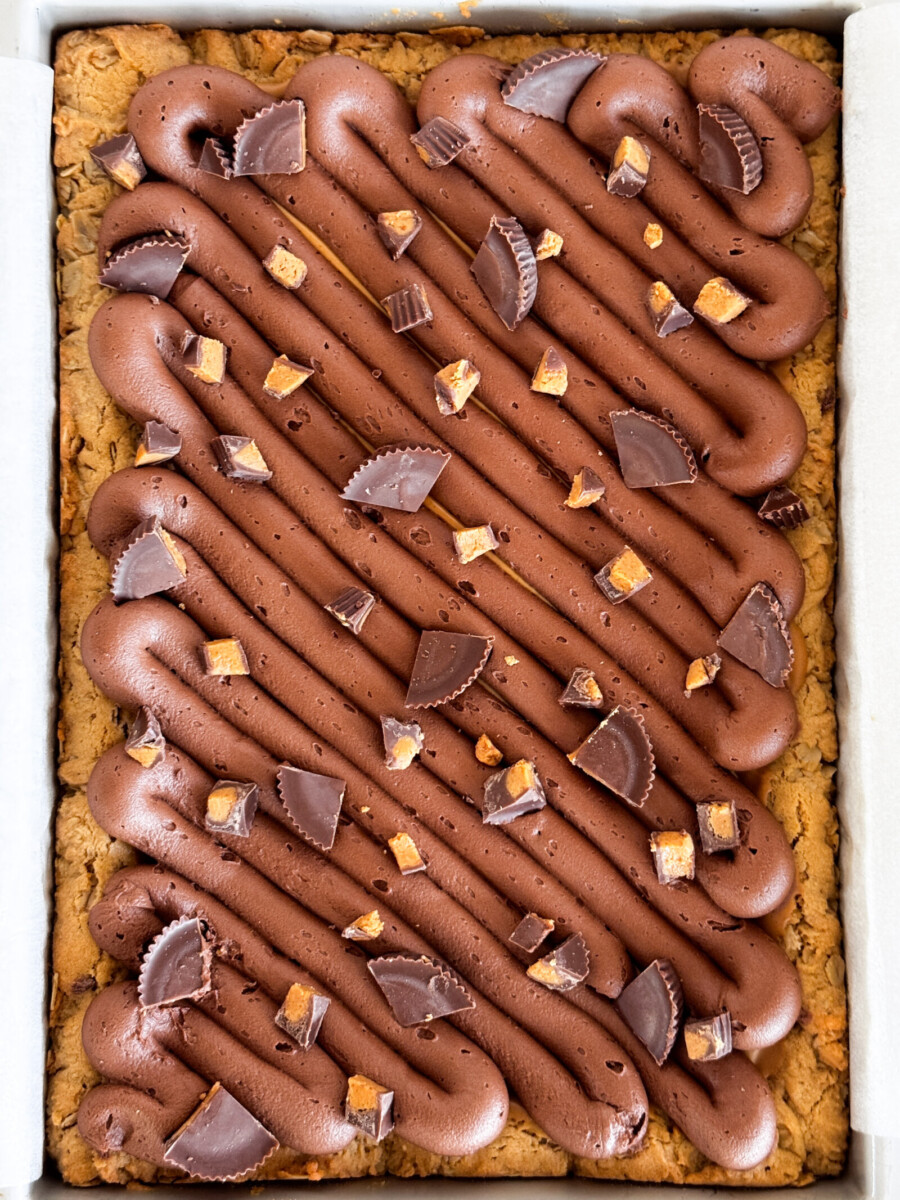 Peanut butter blondies in a pan with chocolate buttercream and Reese's peanut butter cups on top.