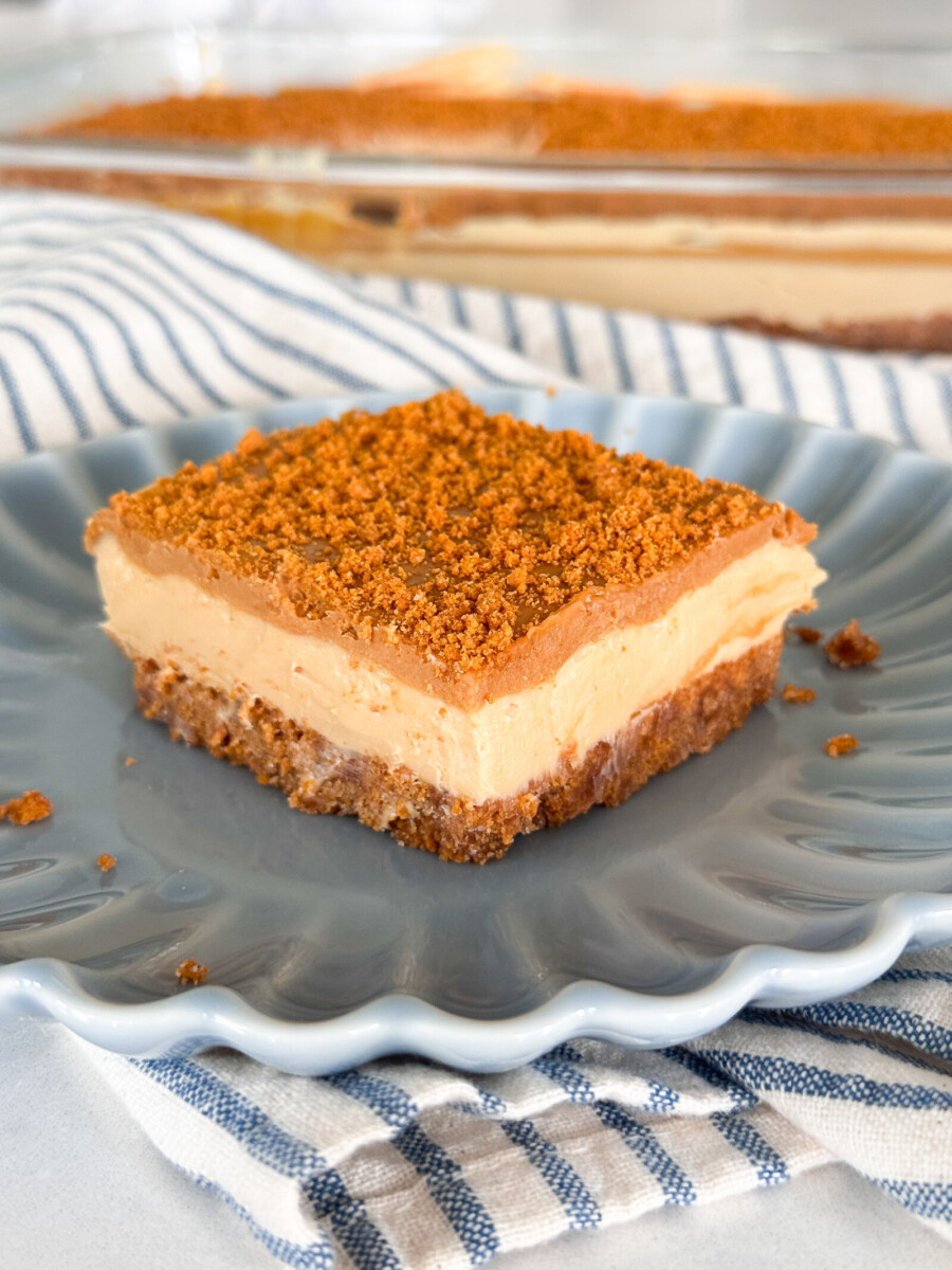 A slice of no-bake Biscoff cheesecake bars on a blue plate with a blue striped napkin.